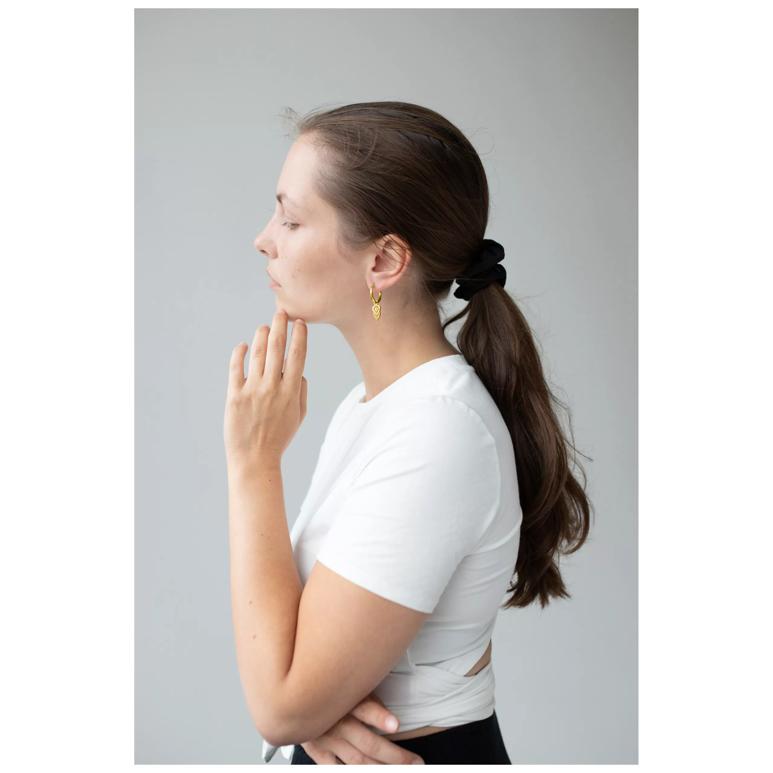 Donna con capelli lunghi indossa orecchini Hoops dorati su sfondo grigio