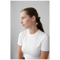Donna con orecchini a cerchio in argento, capelli lisci, maglietta bianca, sfondo neutro