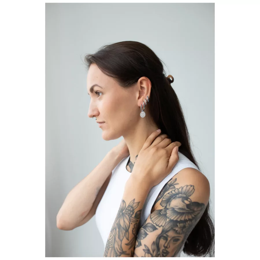 Donna con braccia tatuate indossa orecchini Mandala neri e argento