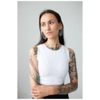Donna con braccia tatuate indossa orecchini Monstera Leaf Hoops, top bianco
