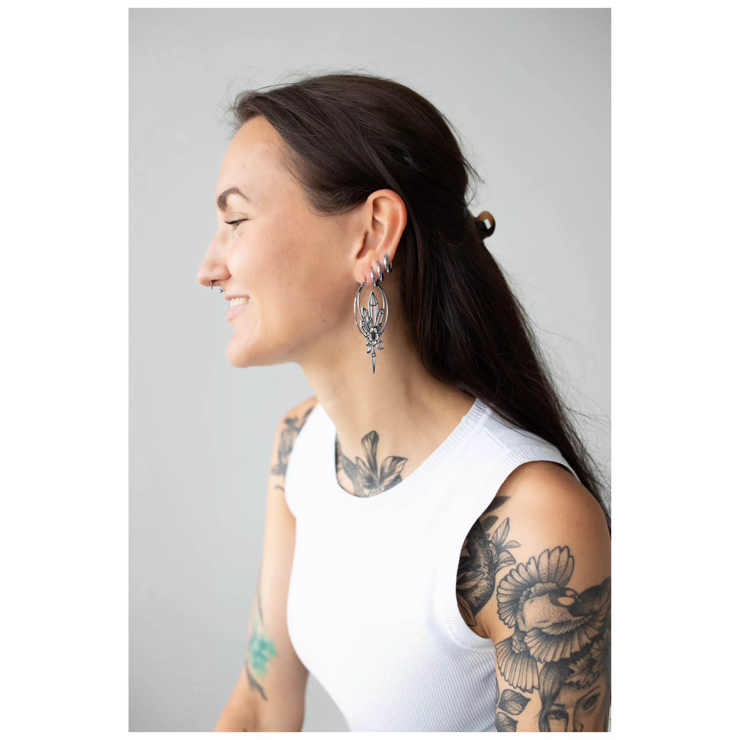 Donna sorridente con orecchini Oracle Hoops in argento su sfondo grigio