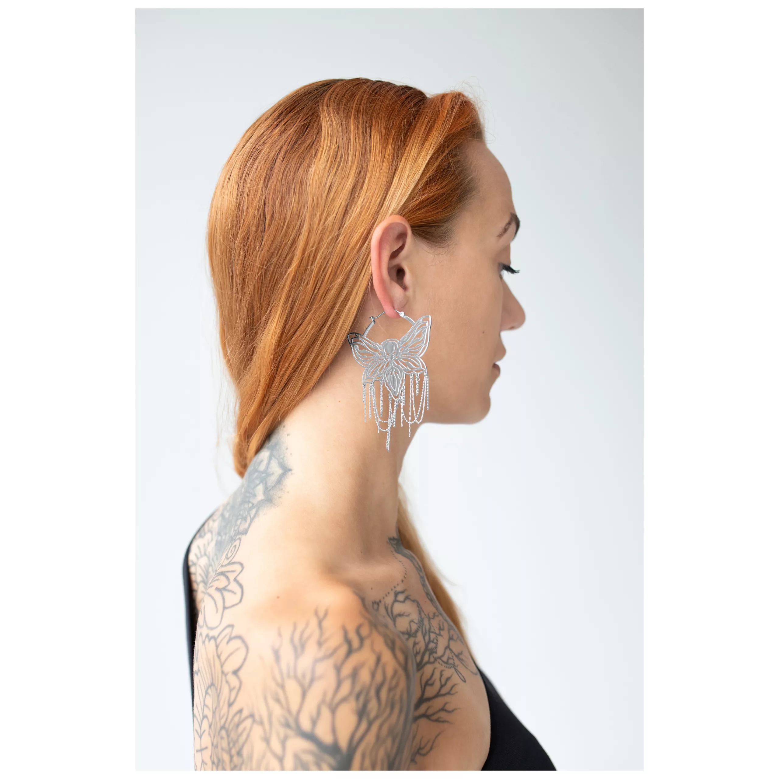 Donna con capelli rossi indossa orecchini a cerchio Moth Chain argento su sfondo bianco