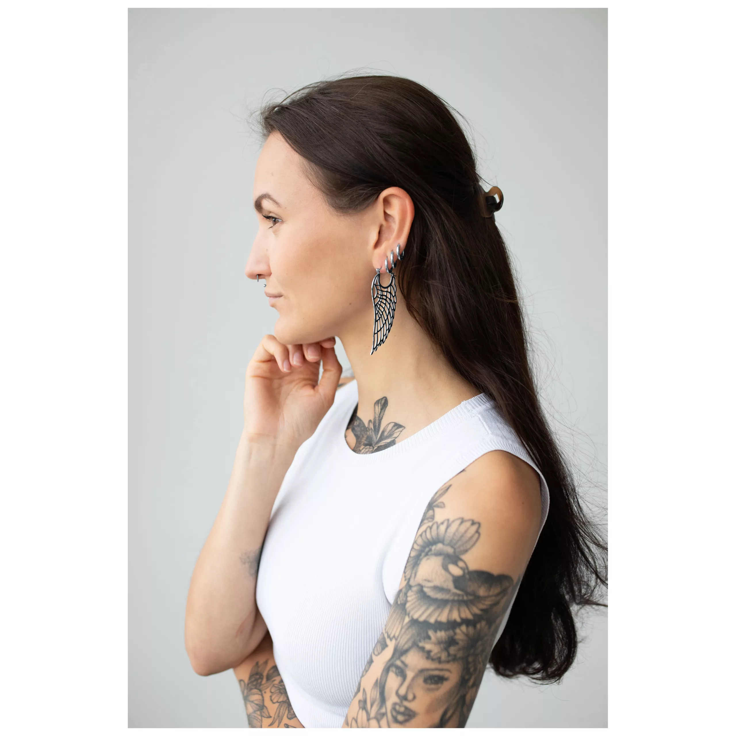 Donna con capelli lunghi indossa orecchini Wing Hoops in argento su sfondo grigio