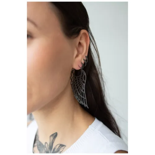 Primo piano di orecchini Wing Hoops neri su un orecchio, indossati da una persona con lunghi capelli scuri