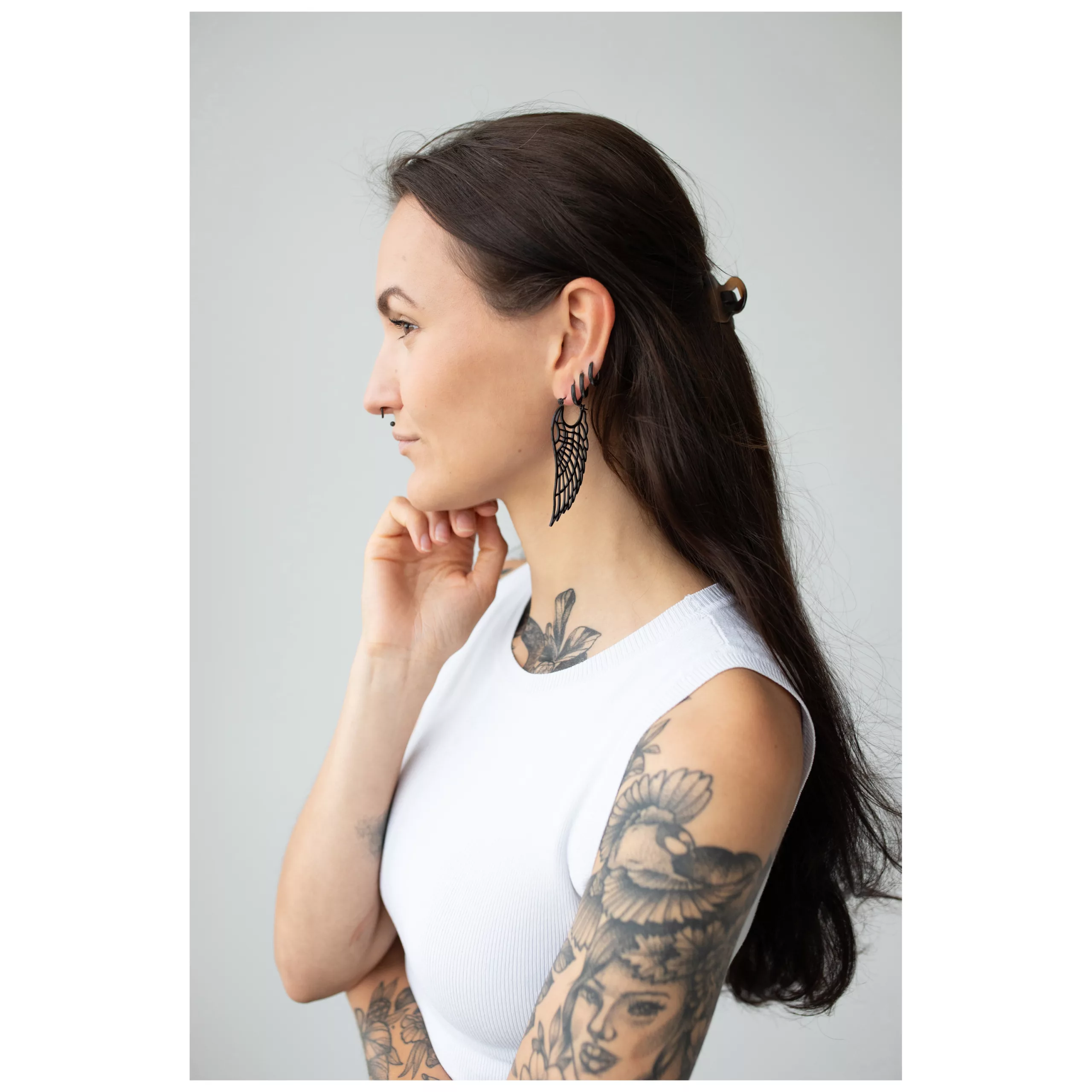 Donna con lunghi capelli scuri, indossa orecchini Wing Hoops neri e una maglietta bianca