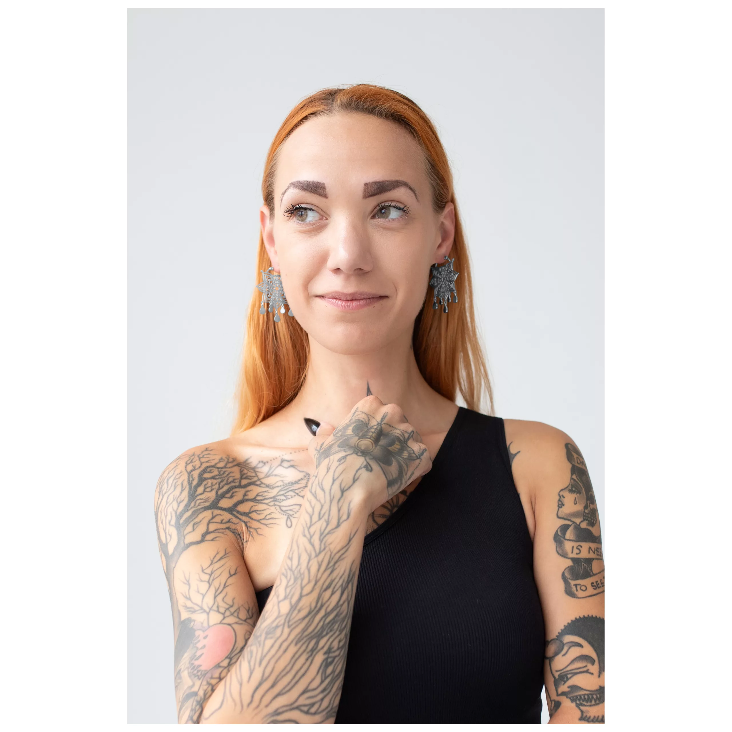Donna con capelli rossi indossa orecchini Mandala in argento, tatuaggi visibili