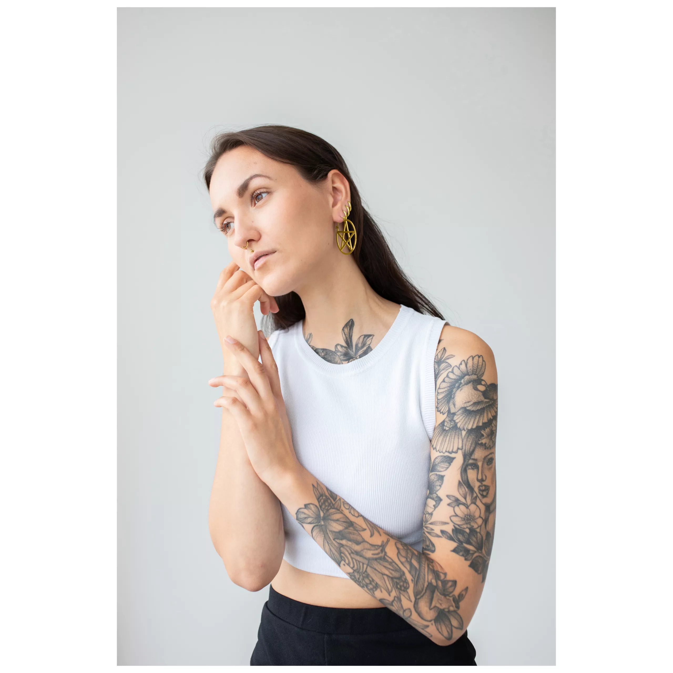 Donna con top bianco indossa orecchini a cerchio pentagramma dorati, tatuaggi visibili