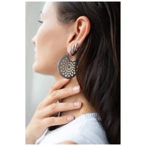 Donna che indossa grandi orecchini rotondi in nero-argento con design filigranato.