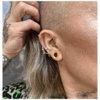 Anello piercing dorato con piccole sfere di cristallo su un orecchio con più piercing.