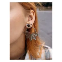 Orecchini Abey Hoops d'argento con motivo a foglia all'orecchio di una donna, sfondo sfocato