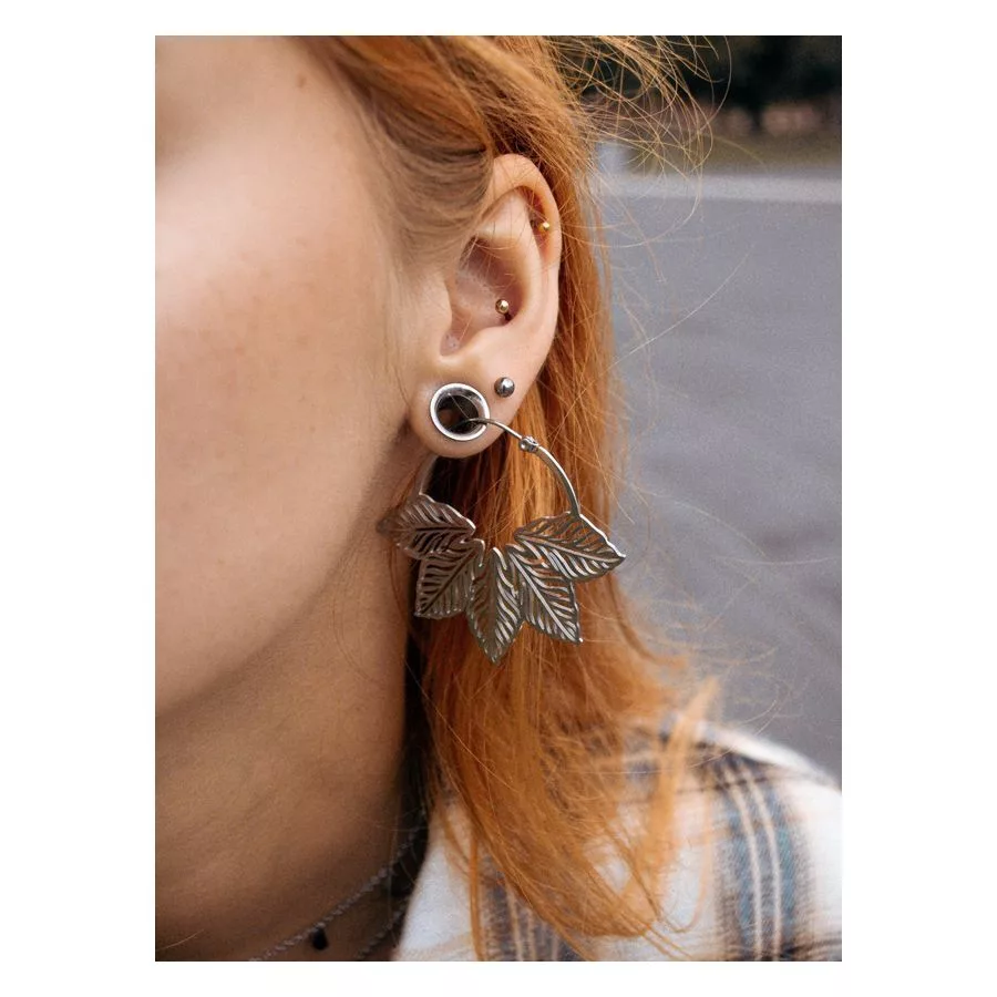 Orecchini Abey Hoops d'argento con motivo a foglia all'orecchio di una donna, sfondo sfocato