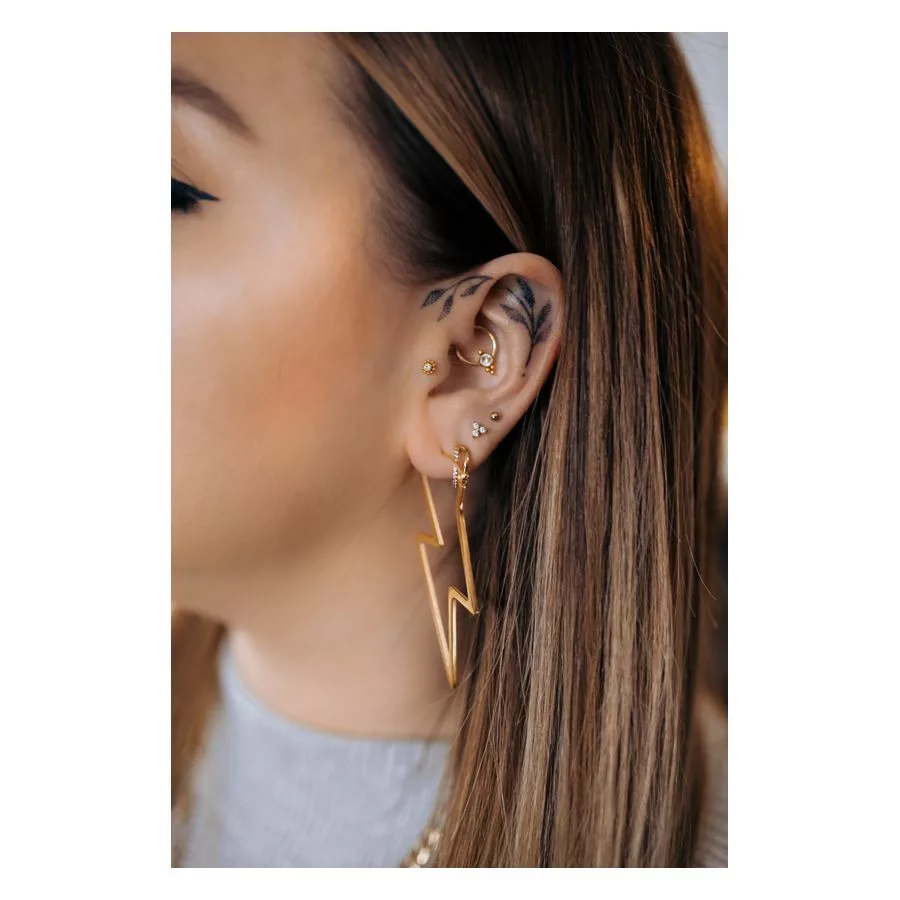 Thunderbolt Hoops orecchini in oro Primo piano di un orecchio con orecchini a fulmine dorati e diversi piercing, sfondo neutro