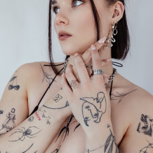 Persona con anello serpente e tatuaggi, indossa gioielli su sfondo bianco