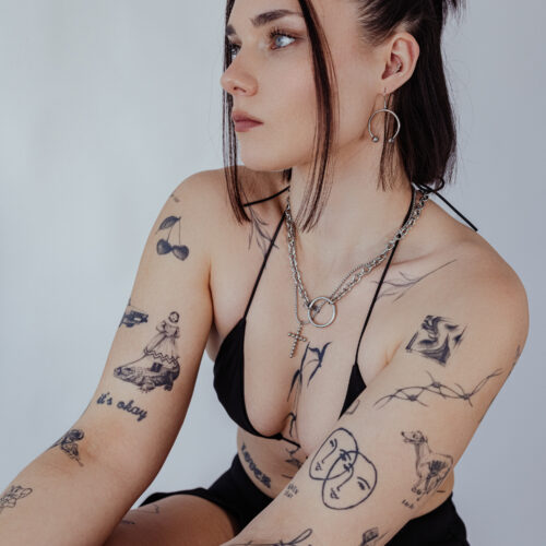 Donna con orecchini Circular Barbell argento e tatuaggi su sfondo chiaro