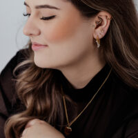Donna con anelli piercing dorati e cristalli all'orecchio su sfondo chiaro