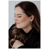 Donna con occhi chiusi indossa un clicker in oro rosa con cristalli a cascata nell'orecchio, su sfondo grigio