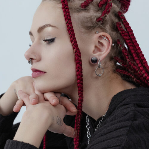 Donna con dreadlocks rossi indossa orecchini d'argento e piercing al naso, profilo laterale
