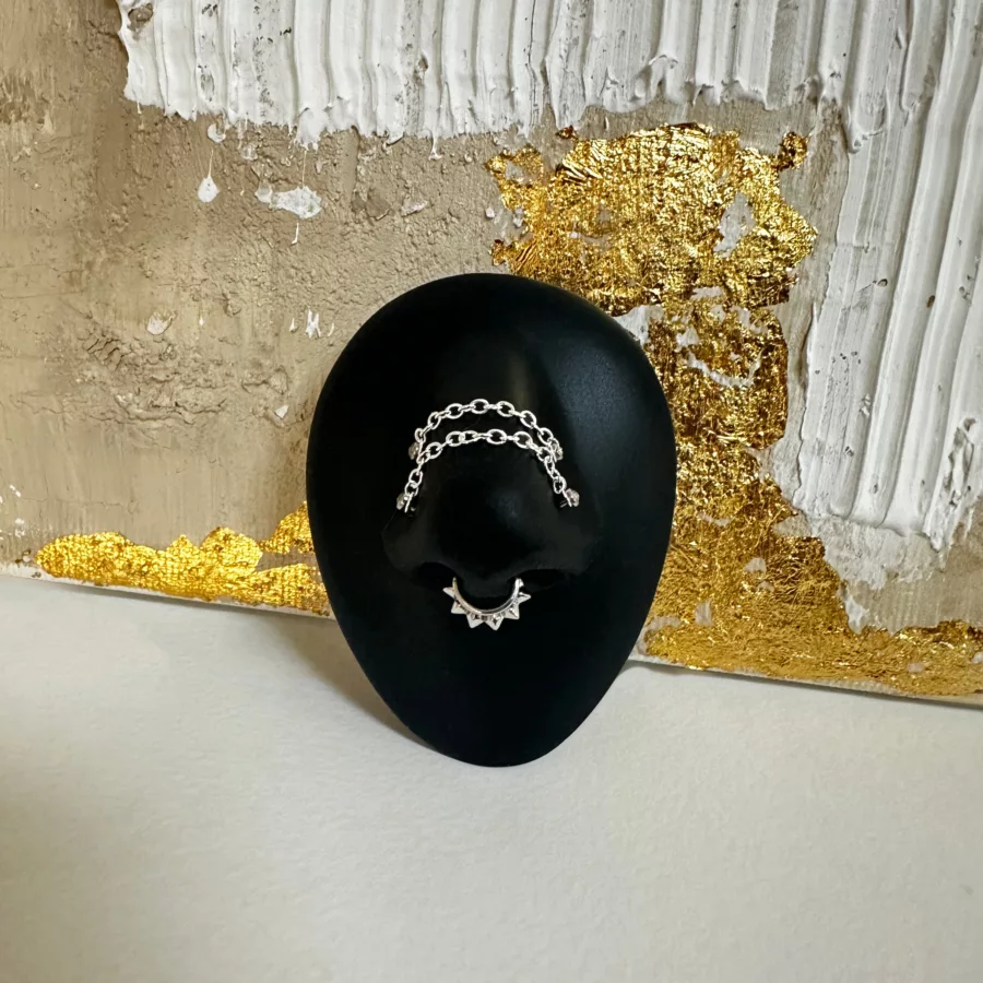 Catena piercing argento su supporto nero davanti a parete oro-bianca