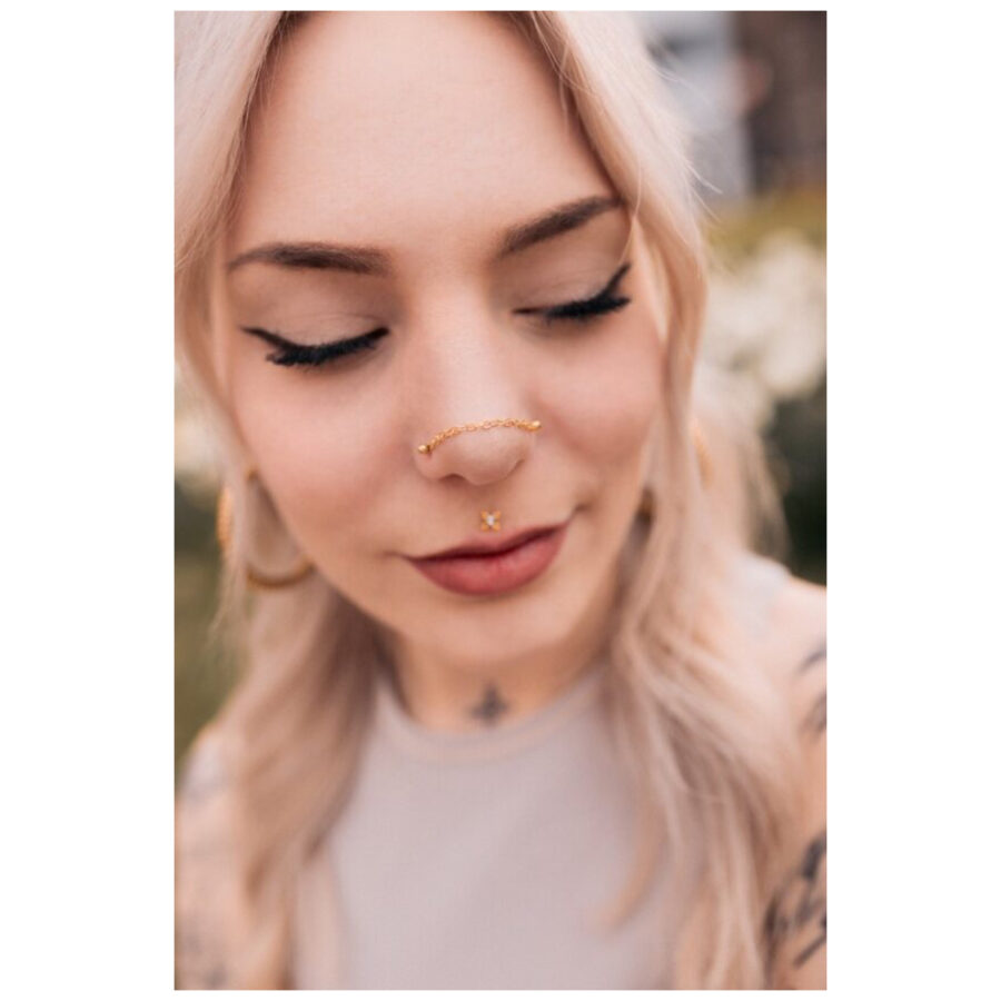 Donna con catena piercing dorata su naso e orecchio, all'aperto