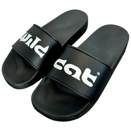 Slides in PVC nere con logo Wildcat bianco su sfondo neutro