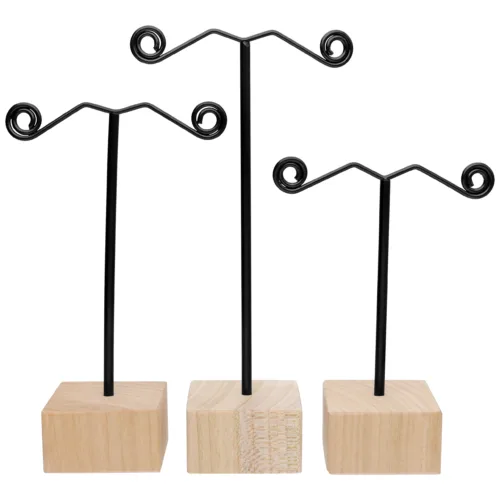 Tre espositori neri per orecchini con base in legno naturale su sfondo bianco
