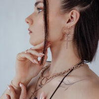 Donna indossa orecchini Bubble Cross Hoops in oro rosa su sfondo neutro