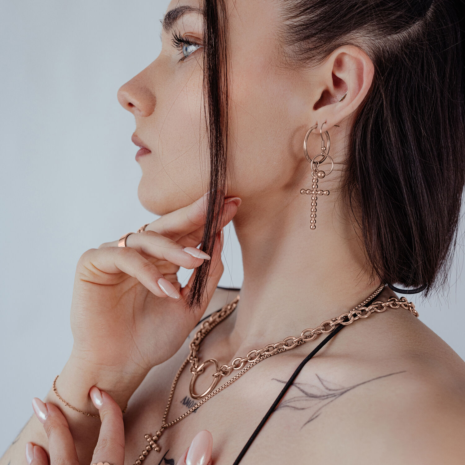 Donna indossa orecchini Bubble Cross Hoops in oro rosa su sfondo neutro