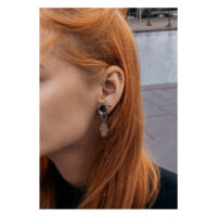 Orecchini a mano Hamsa color argento su un orecchio con lunghi capelli rossi, scattata all'aperto