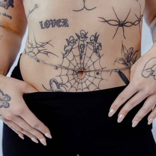 Donna indossa doppie catene per il ventre in argento e oro su pancia tatuata