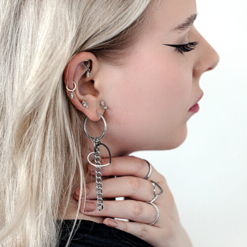 Orecchini a cerchio a cuore in argento e oro all'orecchio di una donna con capelli biondi