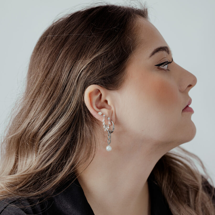 Donna con catena piercing in argento all'orecchio, capelli di lato, sfondo chiaro