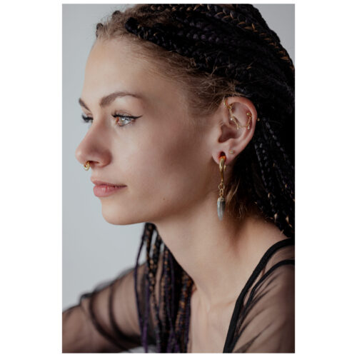 Donna con catena piercing in argento e ciondolo di cristallo all'orecchio, sfondo neutro