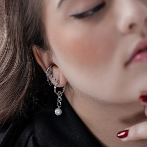 Primo piano di cerchi d'argento con pendente di perla all'orecchio di una persona