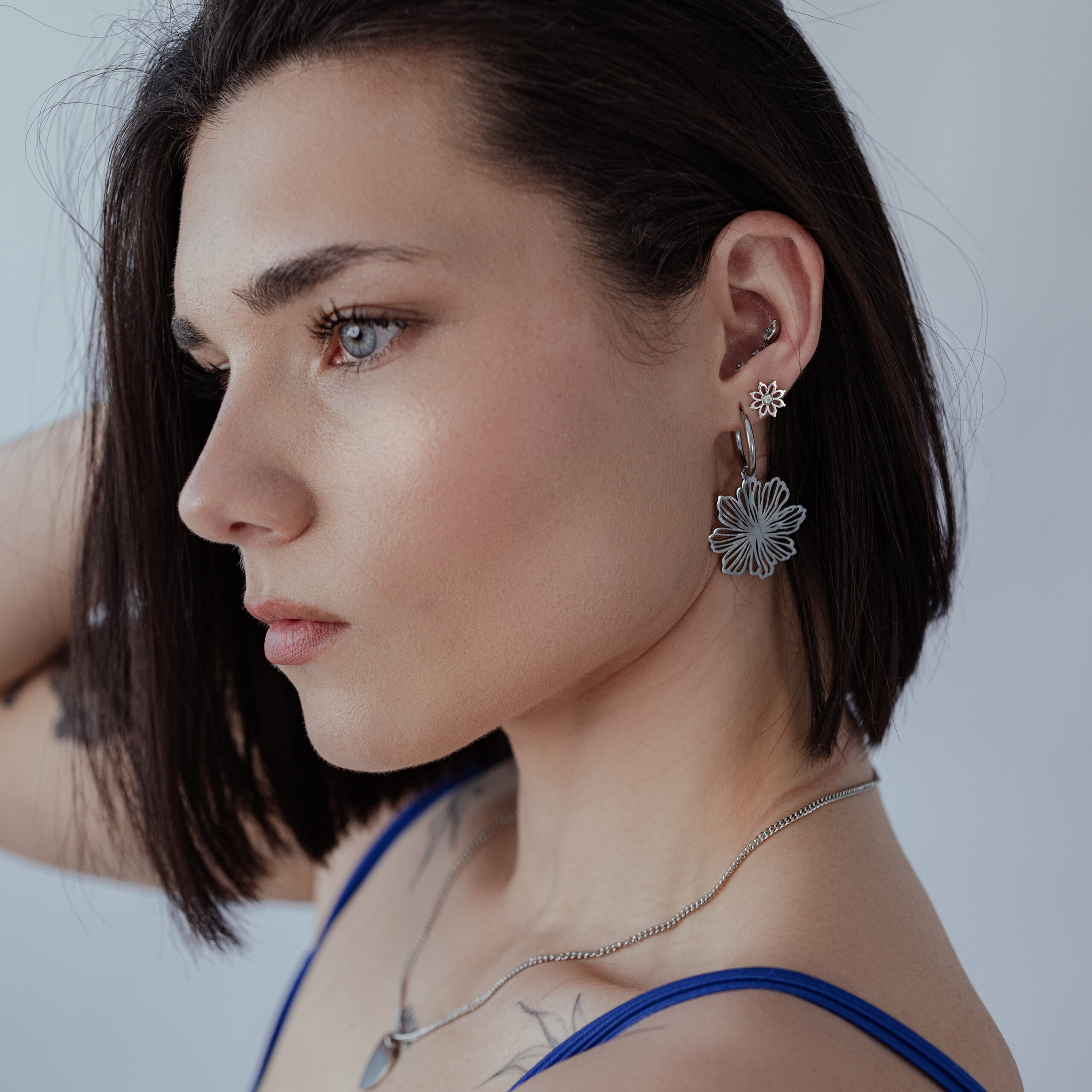 Donna con capelli corti indossa Fine Flower Hoops in argento su sfondo grigio