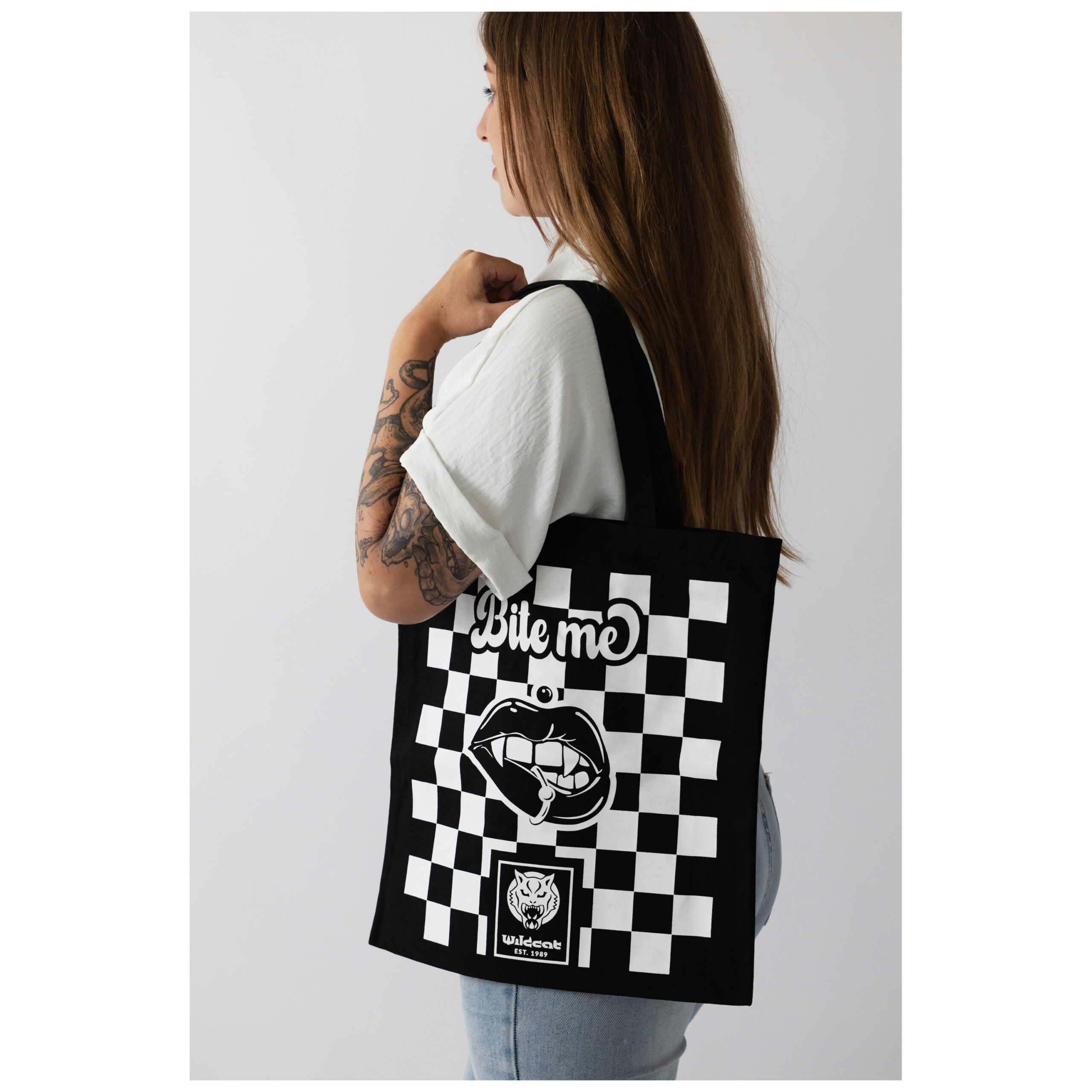 Donna con borsa di cotone nera, motivo a scacchi e scritta 'Bite Me'