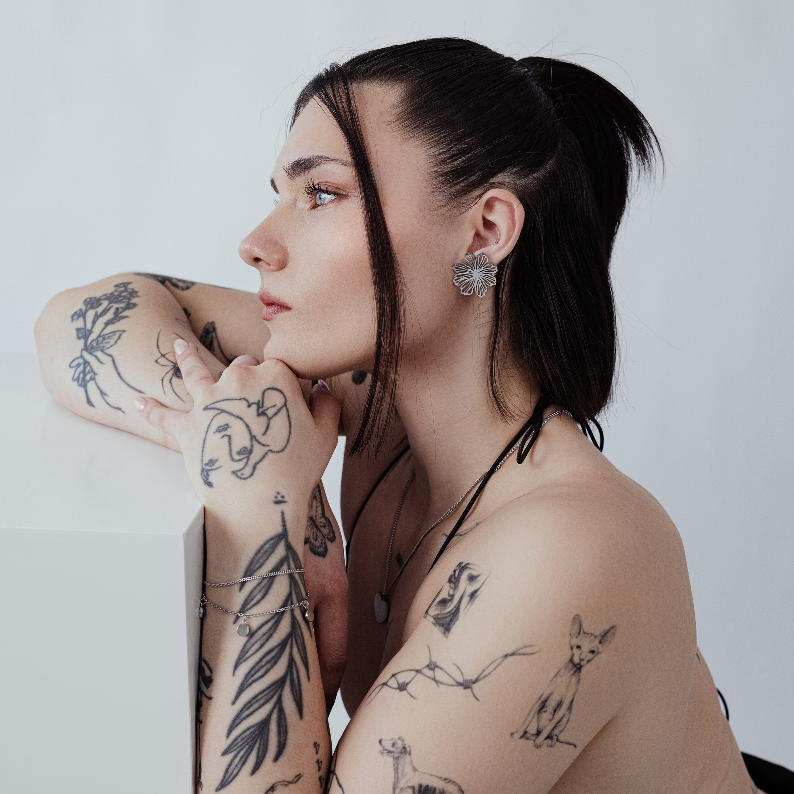 Ritratto laterale di una persona tatuata con eleganti orecchini a fiore, sfondo neutro