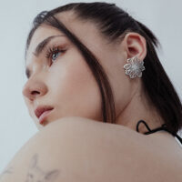 Donna con eleganti orecchini a fiore in acciaio inossidabile argentato su sfondo bianco