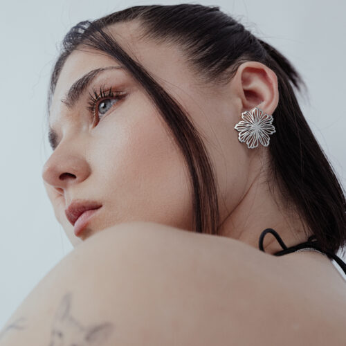 Donna con eleganti orecchini a fiore in acciaio inossidabile argentato su sfondo bianco
