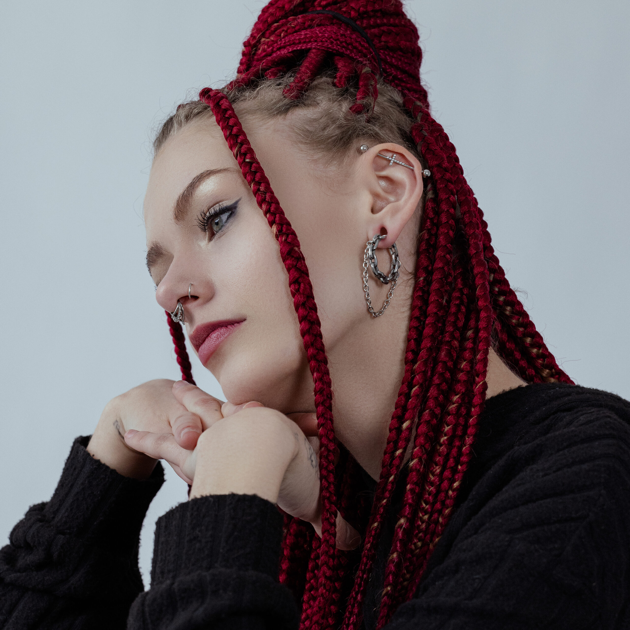 Donna con trecce rosse indossa pesi per orecchie Double Chain in argento e maglione nero su sfondo grigio