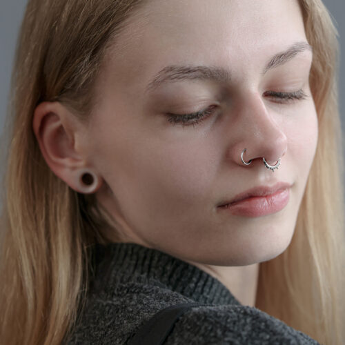 Donna con clicker al setto in argento e lobi allungati su sfondo grigio