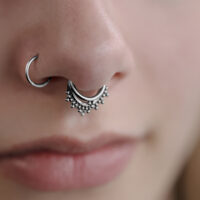 Primo piano di un triplo clicker orientale in argento nel setto di un viso