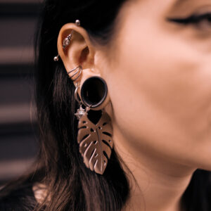 Orecchini Monstera color argento in acciaio chirurgico, indossati all'orecchio di una donna, su sfondo scuro