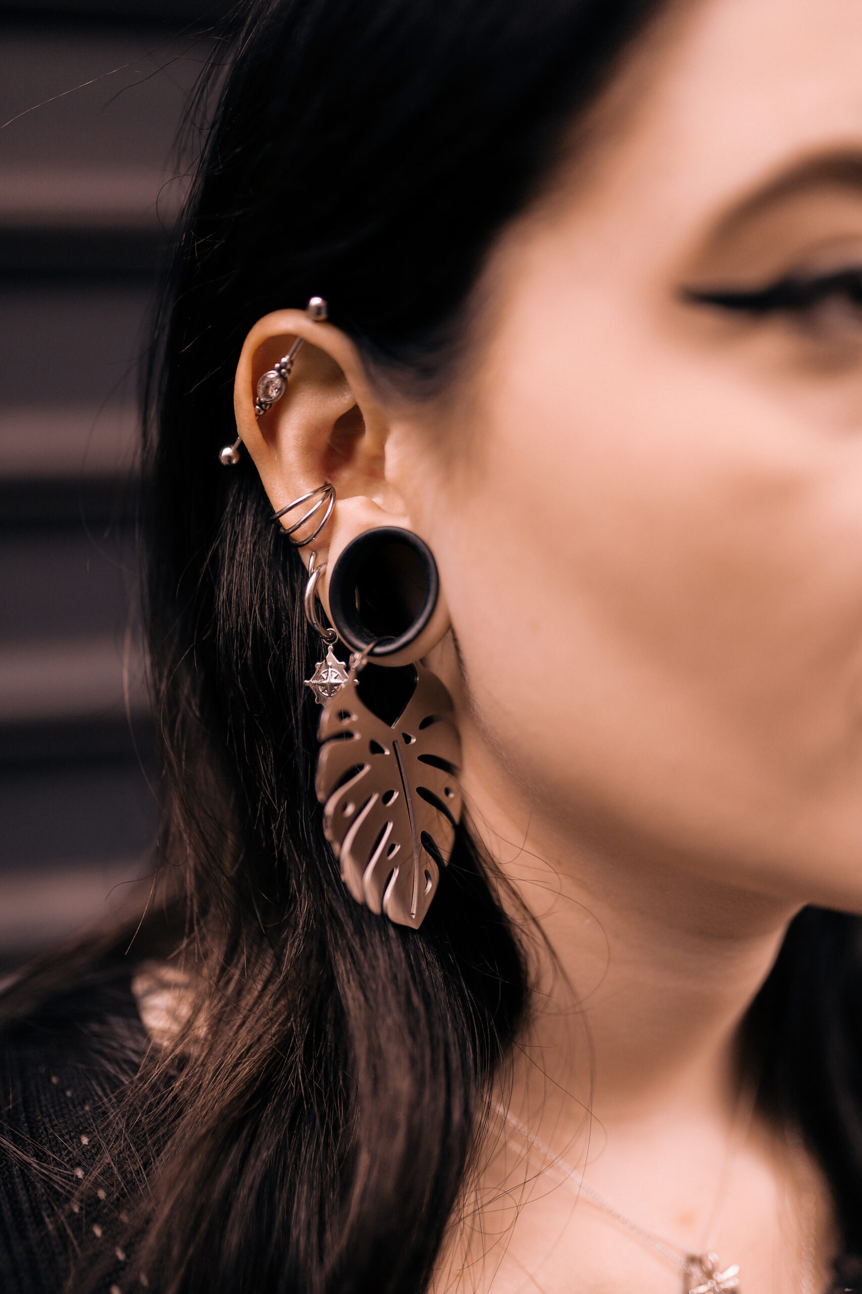 Orecchini Monstera color argento in acciaio chirurgico, indossati all'orecchio di una donna, su sfondo scuro