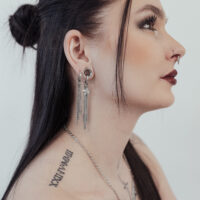 Donna con lunghi capelli neri indossa orecchini Little Shooting Star in argento e ha tatuaggi sul collo.