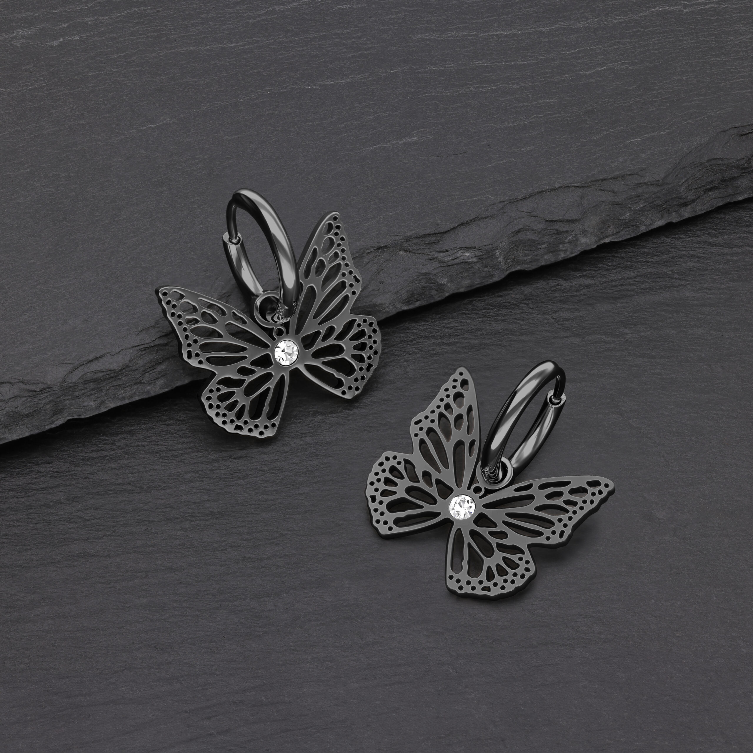 Orecchini a farfalla neri in acciaio chirurgico con cristallo chiaro su sfondo grigio