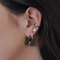 Orecchini neri a forma di farfalla su un orecchio, primo piano della pelle