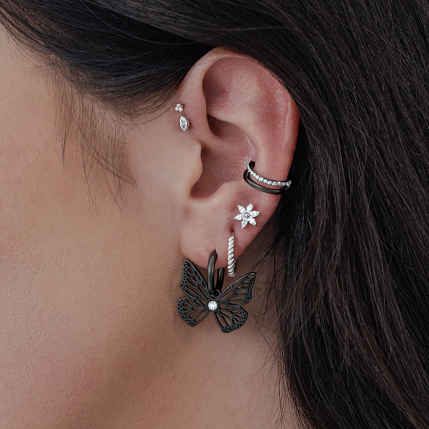 Orecchini neri a forma di farfalla su un orecchio, primo piano della pelle