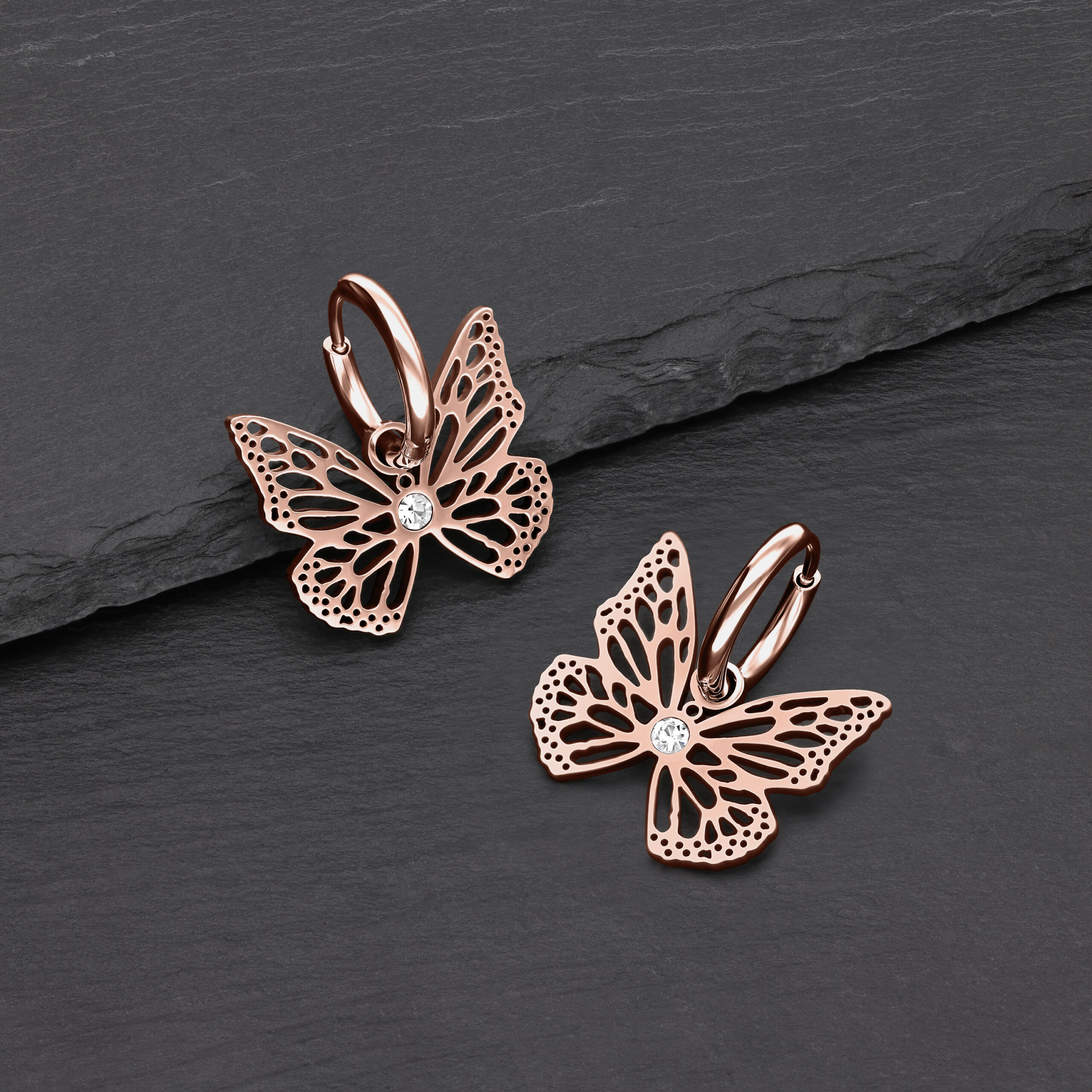 Due orecchini in oro rosa a forma di farfalla con cristalli chiari su sfondo nero
