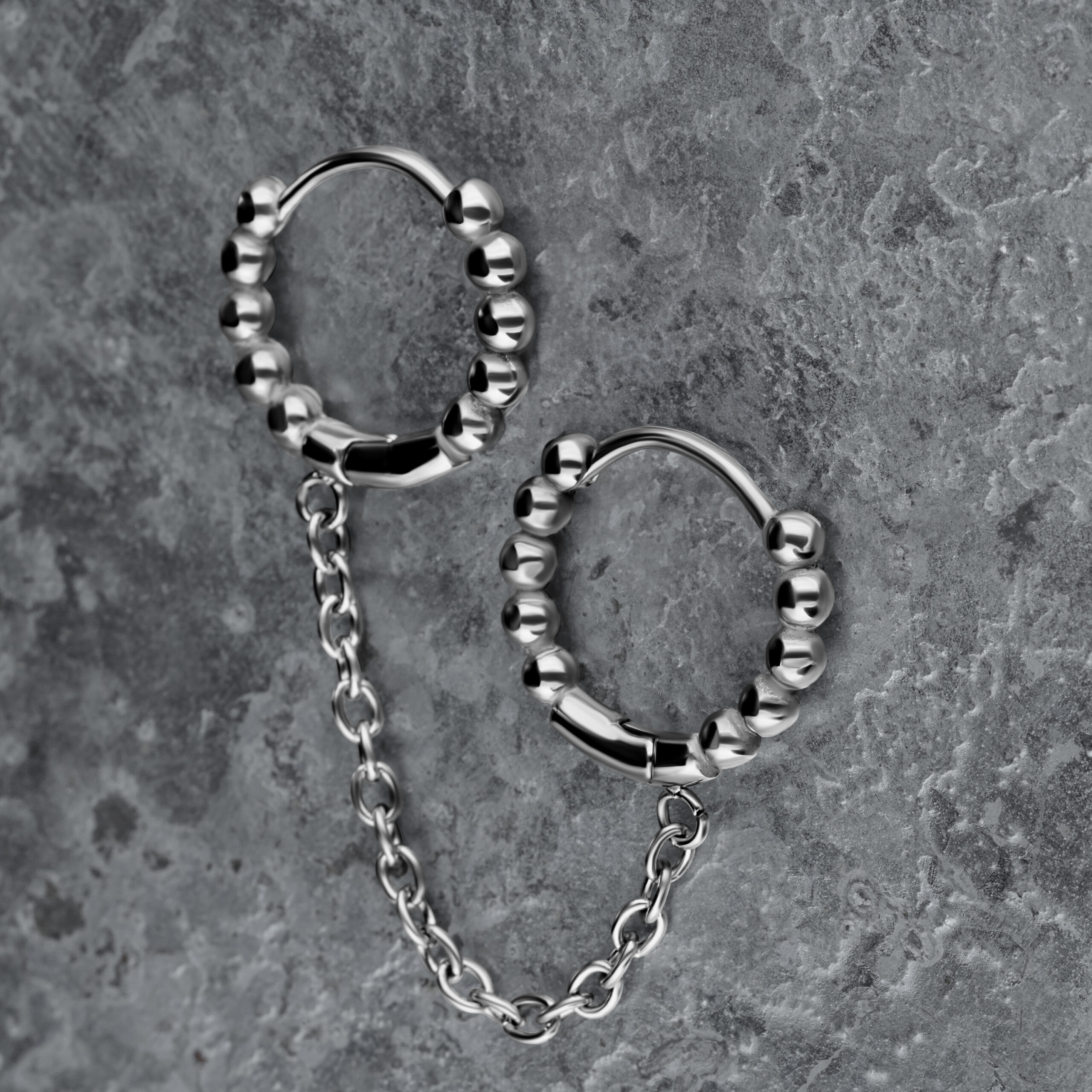 Orecchini doppio Huggie in argento con sfere e catena su sfondo grigio