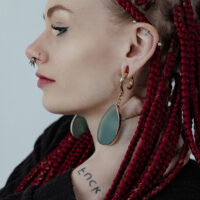 Pesi per orecchie dorati con pietra verde Donna con trecce rosse indossa pesi per orecchie dorati con pietra verde.